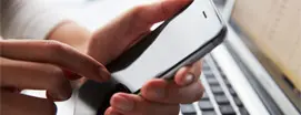 Hands using smartphone near laptop